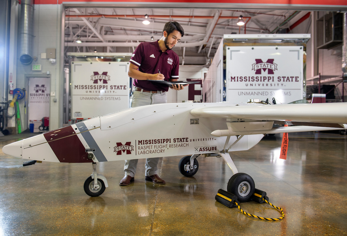 A man stands inside a hangar alongside an unmanned aircraft inside.