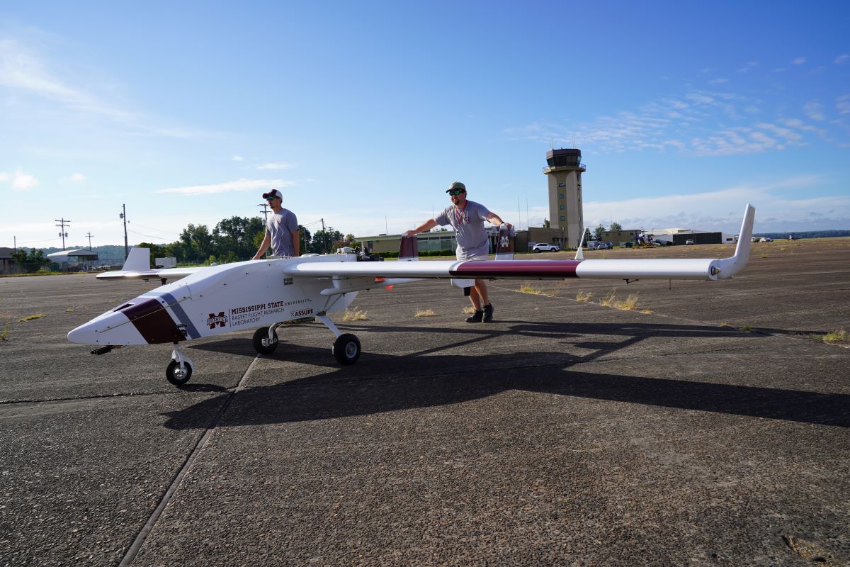 Two technicians push an unmanned aircraft system across a tarmac.