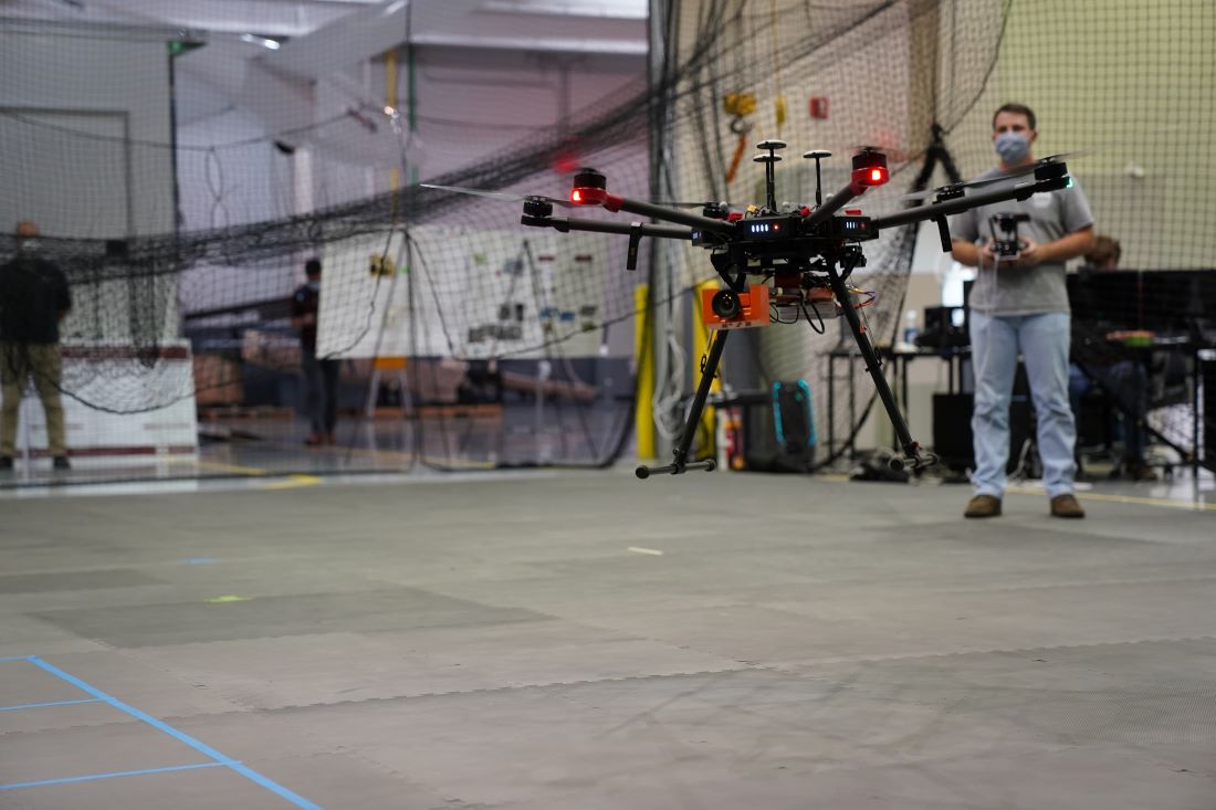 A remote pilot operates a small UAS inside a lab equipped with a netted area for safety.  